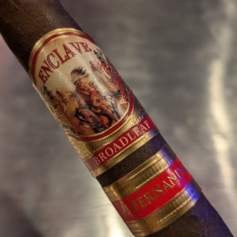 A dark broadleaf maduro AJ Fernandez Enclave cigar wearing three stacked bands: the Enclave crest, a Broadleaf band and an A. Fernandez footband.
