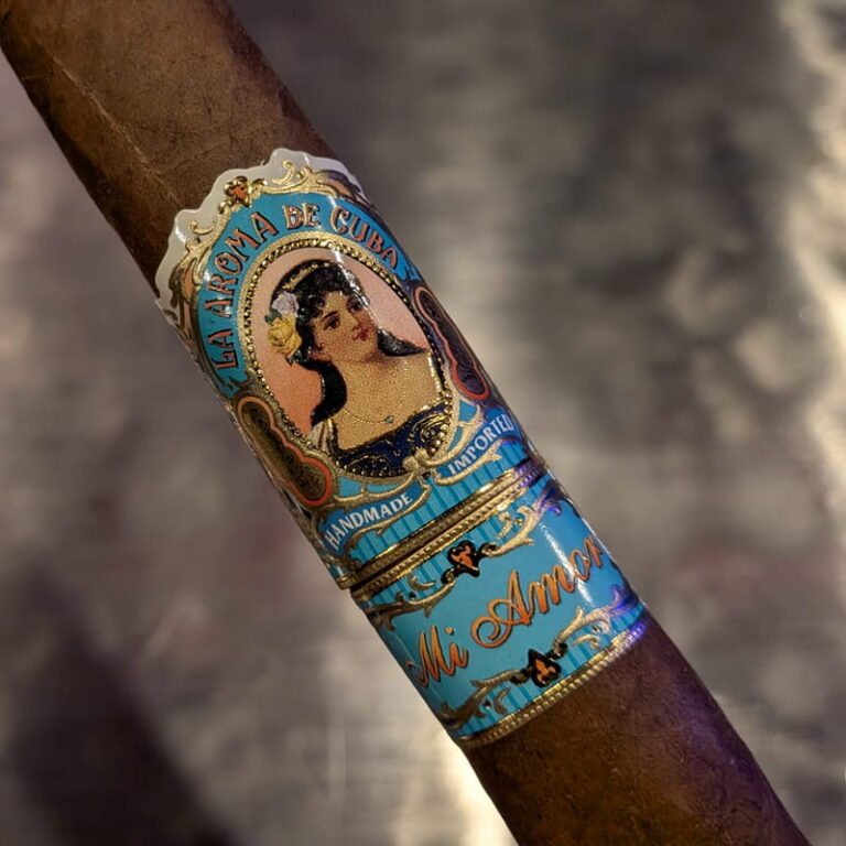 Close macro of a La Aroma de Cuba Mi Amor cigar, its pale blue and gold band carrying an oval cameo portrait above a second Mi Amor band.