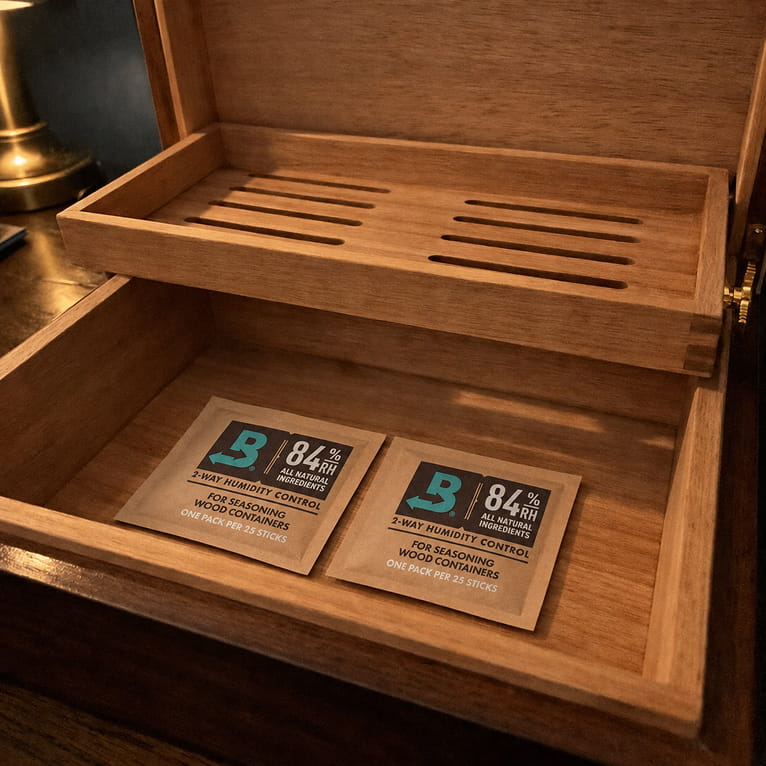 Empty Spanish cedar humidor with its slotted tray raised and two white humidity packets resting flat on the cedar floor