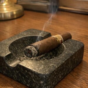 A cigar resting in a heavy stone ashtray with a thin ribbon of smoke rising on a walnut desk